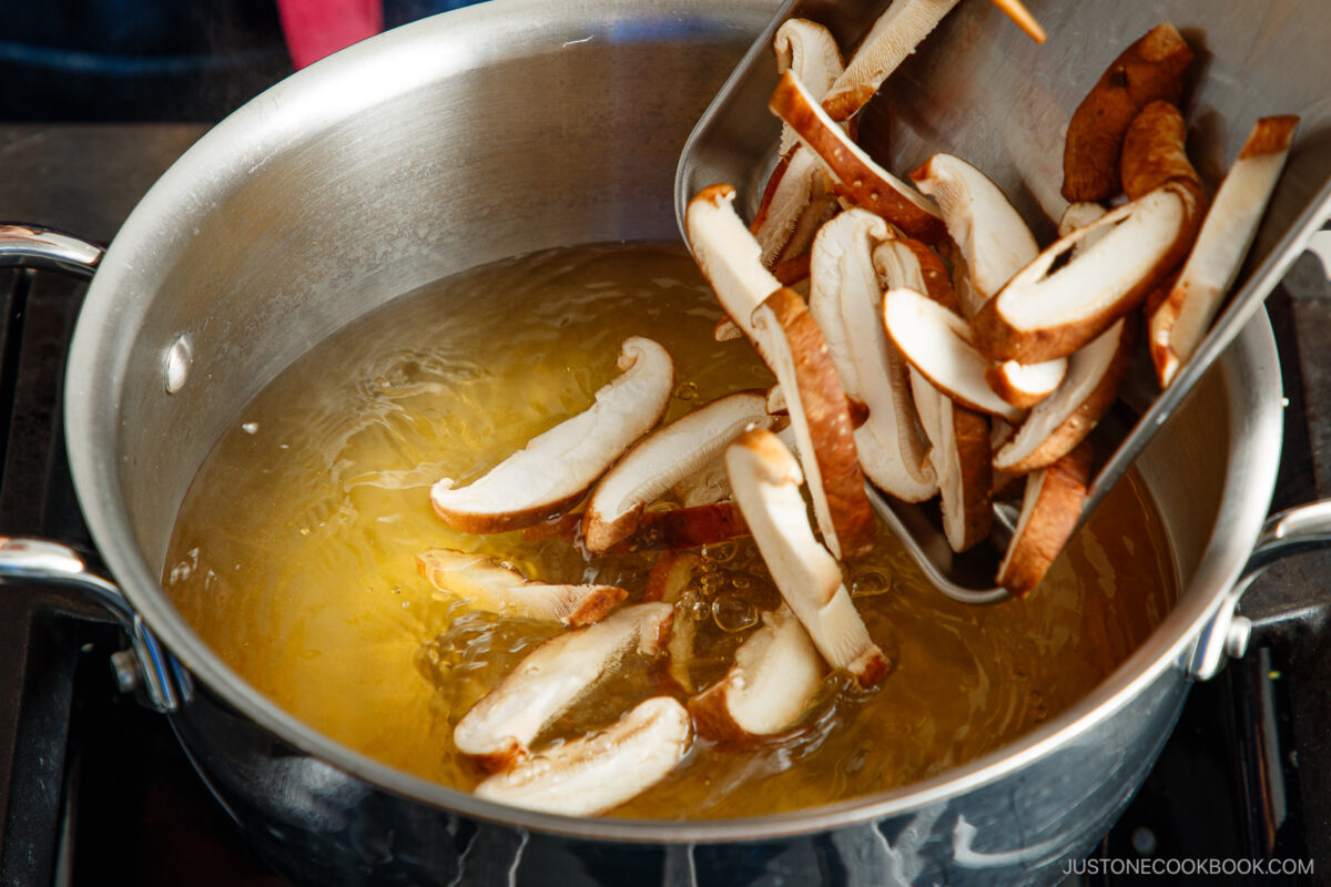 Adding the shiitake mushrooms to the dashi in the pot.