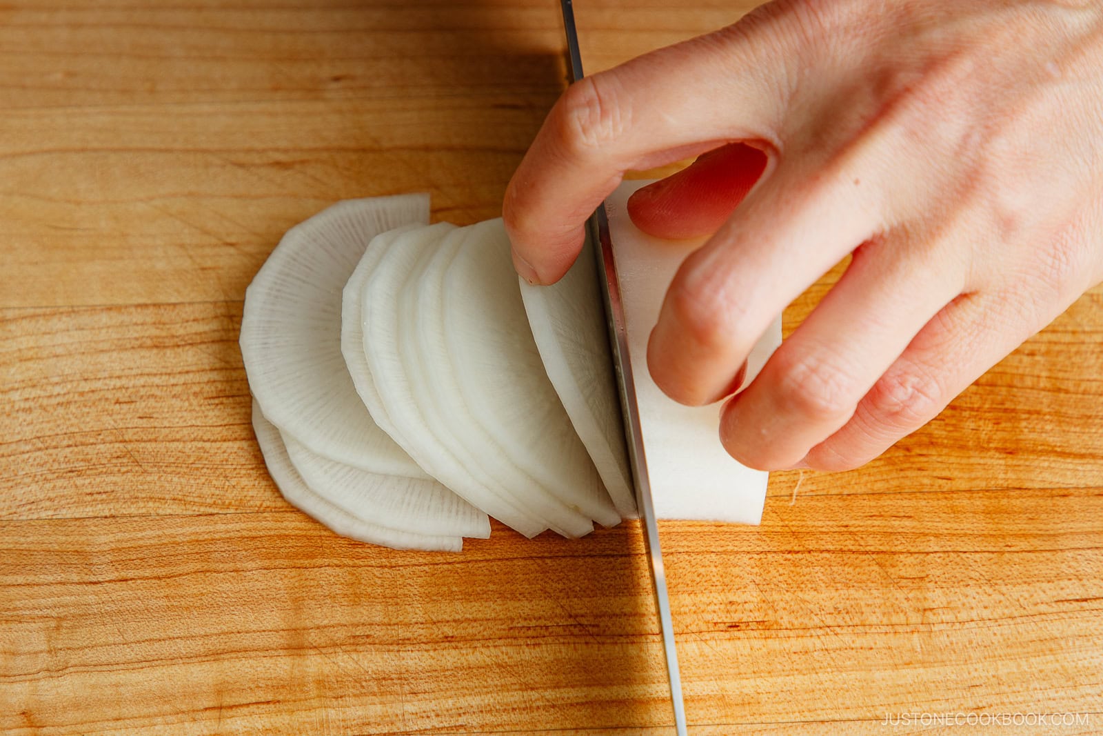Cross-cutting halved daikon into half-moon shapes.