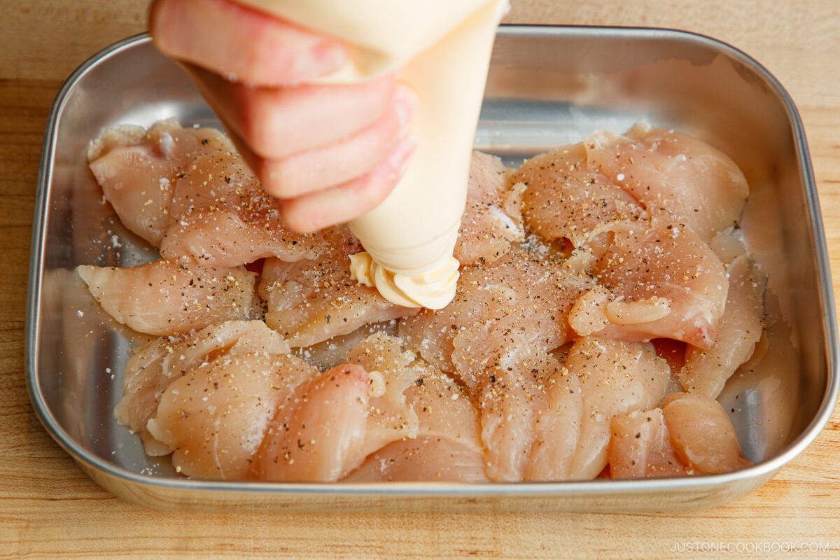 Seasoning the chicken with salt, black pepper, and mayonnaise.