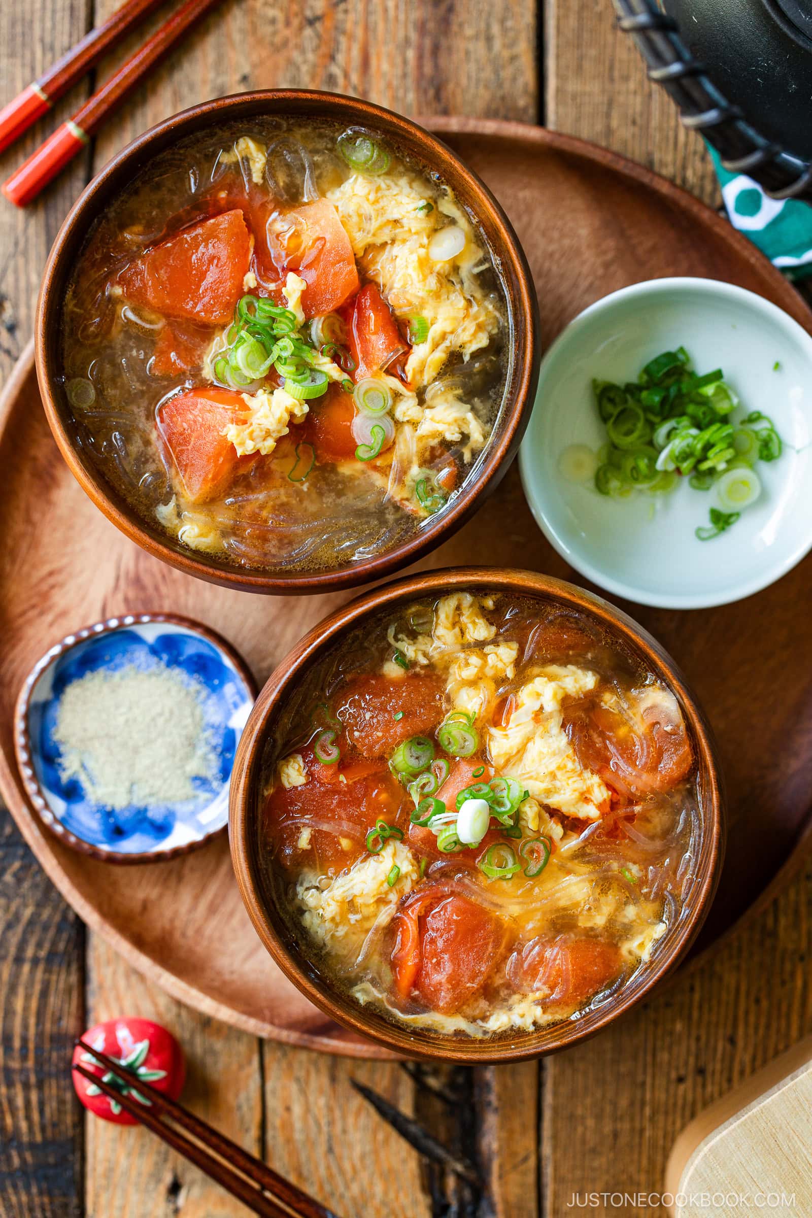 Wooden bowls containing tomato egg vermicelli soup garnished with green onion.