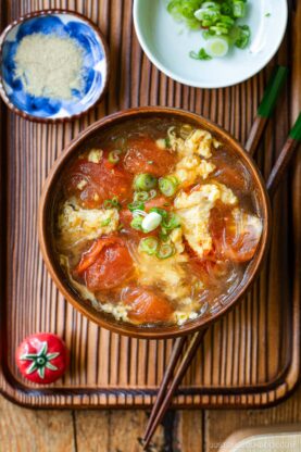 A wooden bowl containing tomato egg vermicelli soup garnished with green onion.