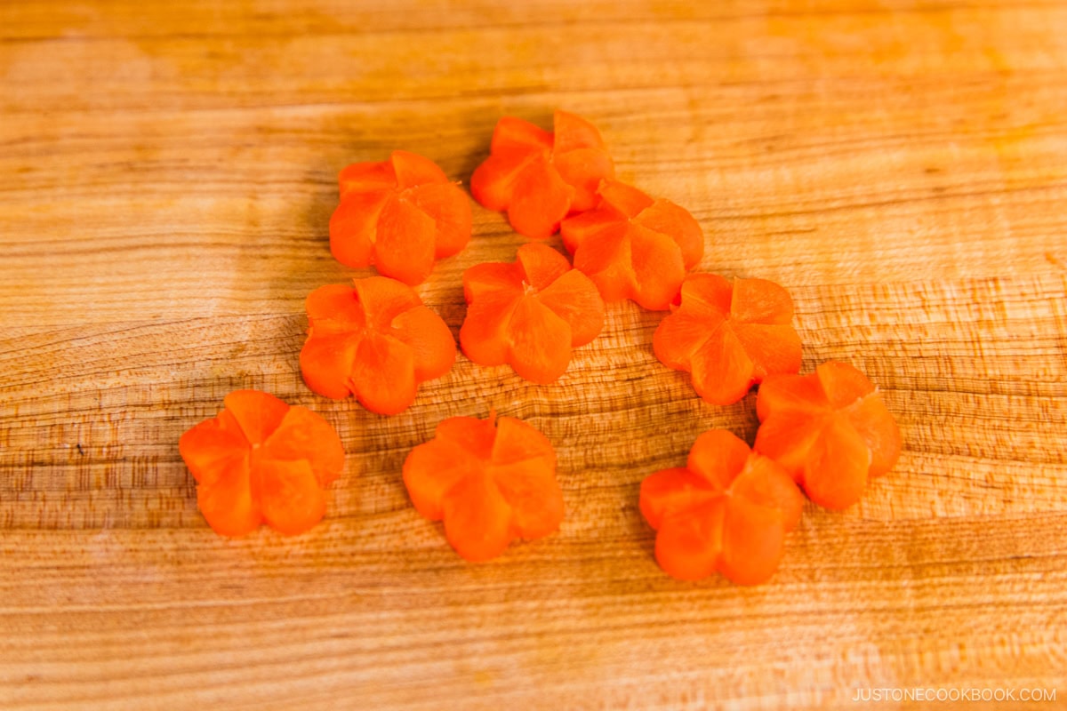 Several thin slices of carrot cut into small, decorative flower shapes are arranged on a wooden cutting board.
