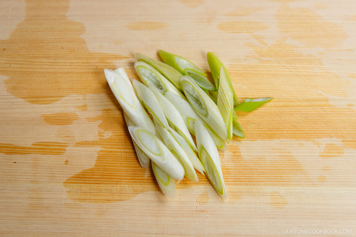Thinly sliced green onions (scallions) arranged on a light wooden cutting board.