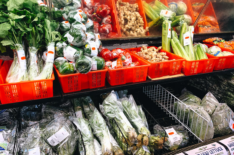 Fresh assorted vegetables including bok choy, bell peppers, celery, and ginger, displayed in red baskets at a grocery store. Perfect for Asian cuisine recipes.