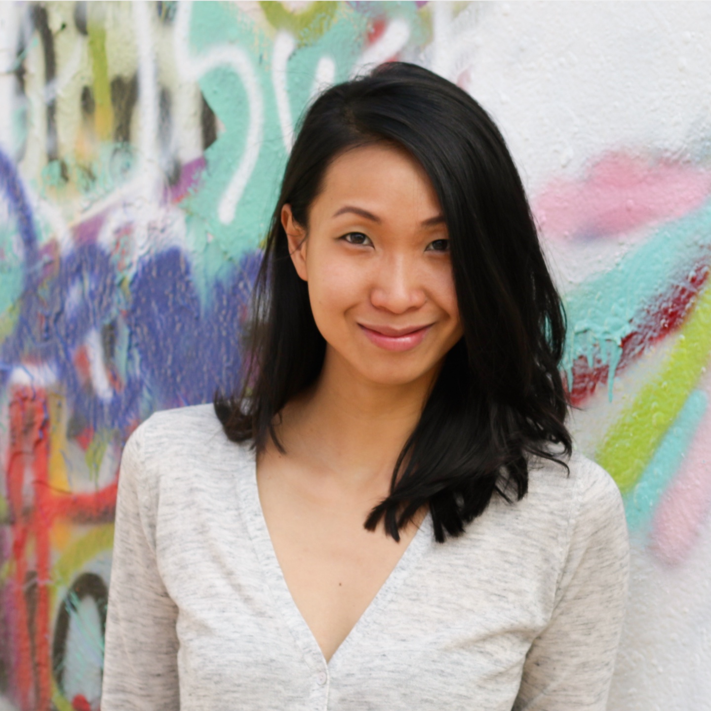 Vibrant street art background with a smiling woman with long black hair, casual beige top, highlighting urban culture and contemporary style.