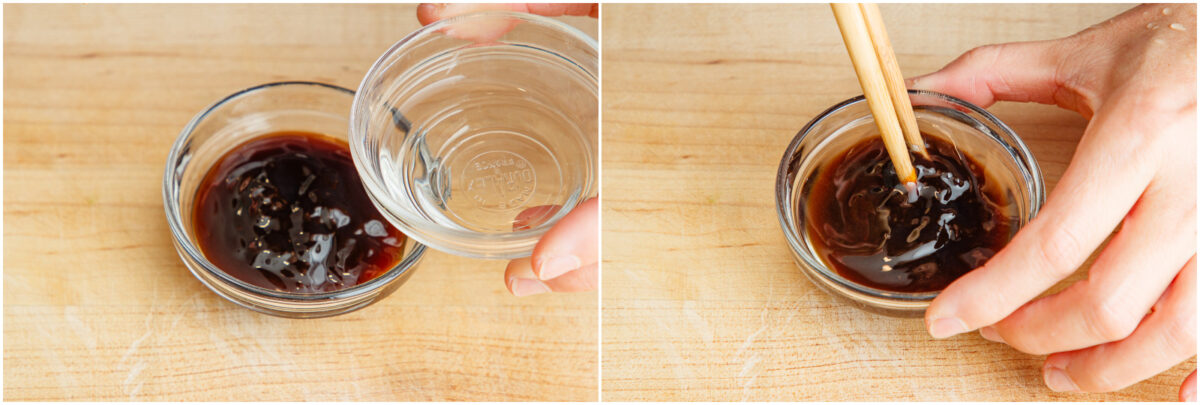 A hand pours liquid from a small bowl into another bowl containing a dark sauce, then stirs the mixture with chopsticks on a wooden surface.