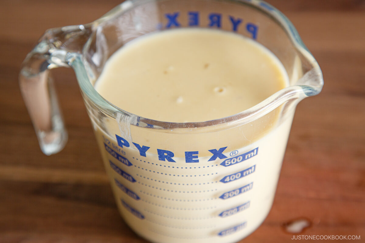 A glass Pyrex measuring cup filled with creamy yellow liquid sits on a wooden surface. The liquid reaches close to the 600 ml mark on the cup.