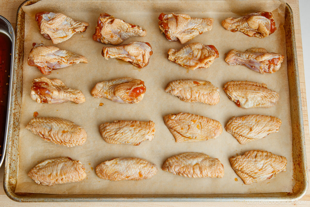 Raw chicken wings arranged in neat rows on a parchment-lined baking sheet, ready to be cooked.