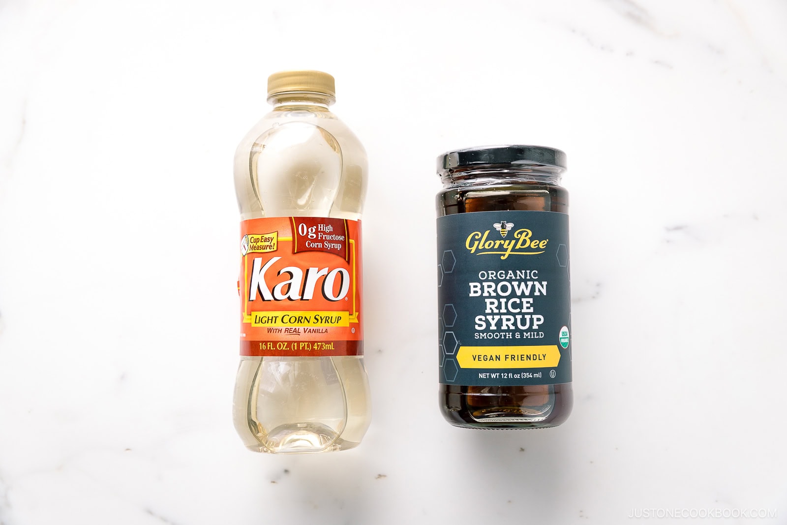A bottle of Karo light corn syrup and a jar of GloryBee organic brown rice syrup are placed side by side on a white marble surface.