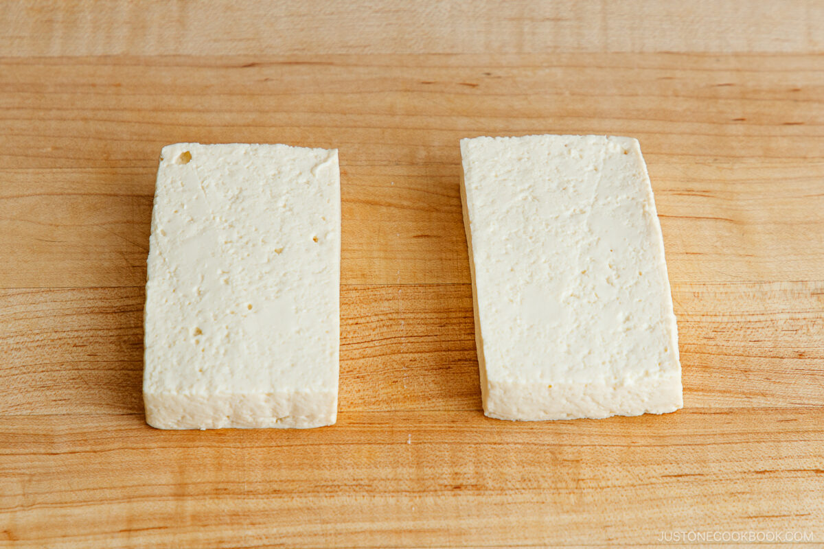 Two rectangular slices of tofu placed side by side on a wooden cutting board.
