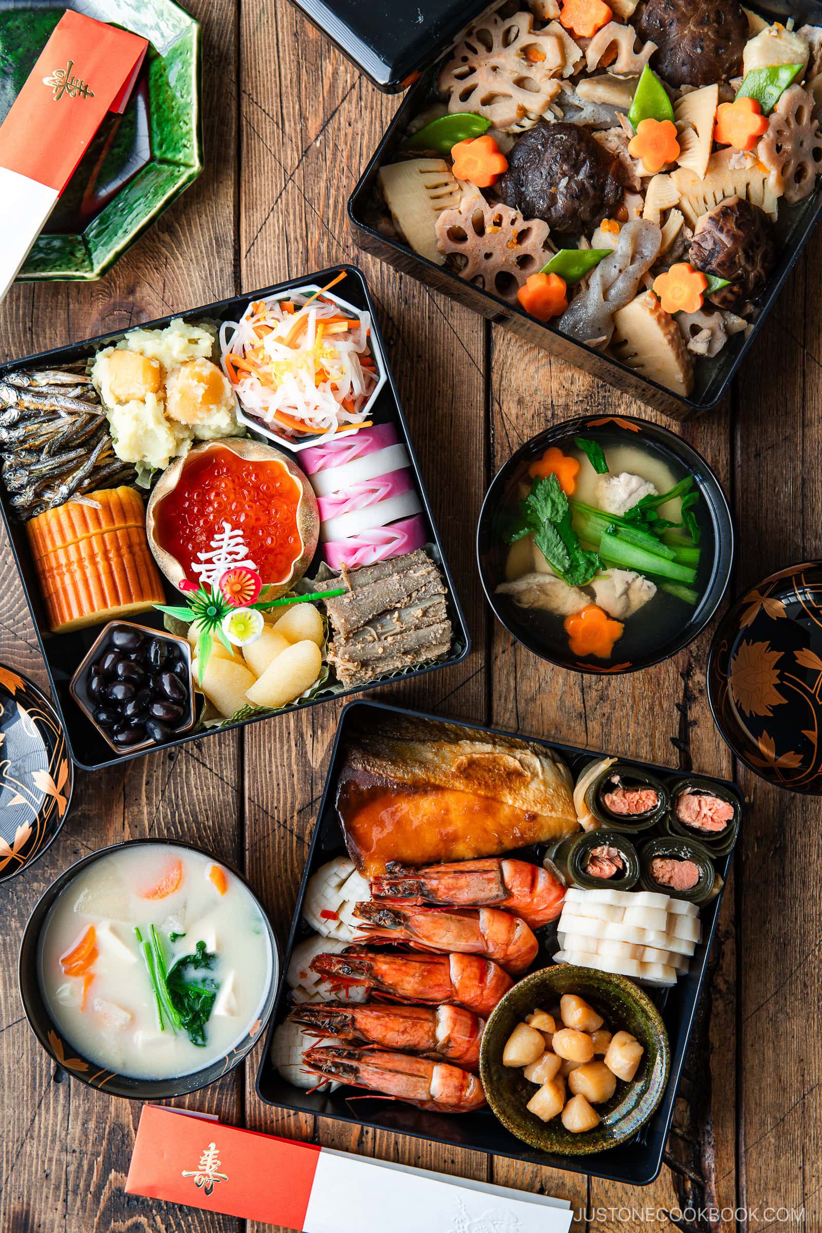 A top-down view of traditional Japanese osechi ryori New Year’s food in lacquer boxes, featuring shrimp, fish, vegetables, egg roll, black beans, and soups, all beautifully arranged with decorative garnishes.