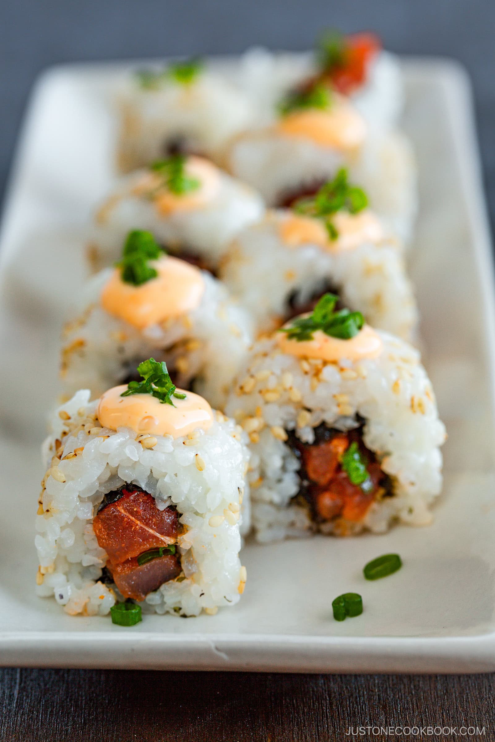 Close-up of spicy tuna rolls topped with a dollop of spicy mayo and garnished with chopped green onions, beautifully arranged on a white rectangular plate.