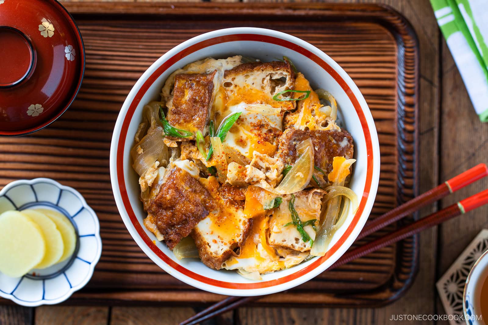 A bowl of Simmered Tofu and Egg Rice Bowl with tofu, softly cooked eggs, and onions simmered in a savory sauce, then spooned over steamed rice—placed on a wooden tray with pickled ginger, chopsticks, and a miso soup bowl nearby.