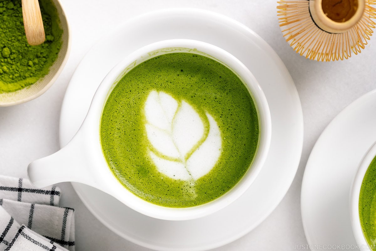 White cup and saucer containing Matcha Latte with tulip latte art.