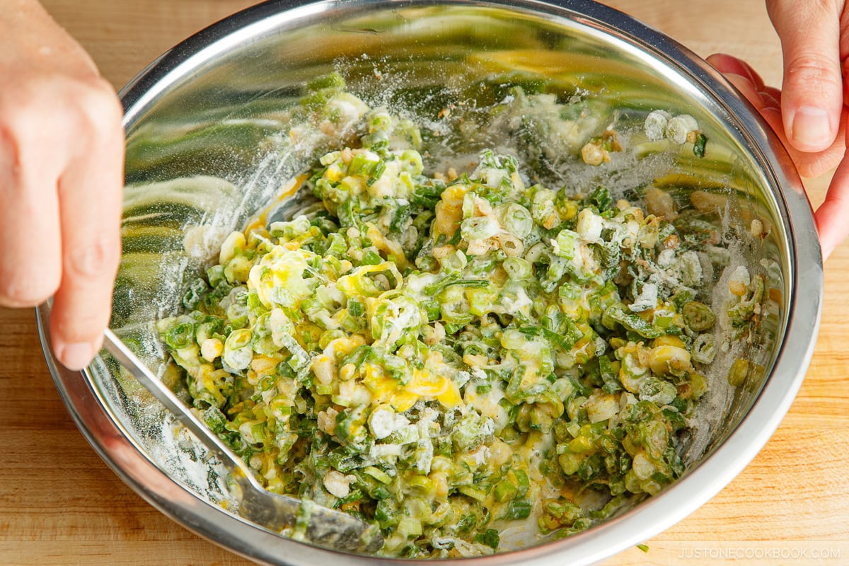 A stainless steel mixing bowl containing negiyaki batter mixed with a spoon.