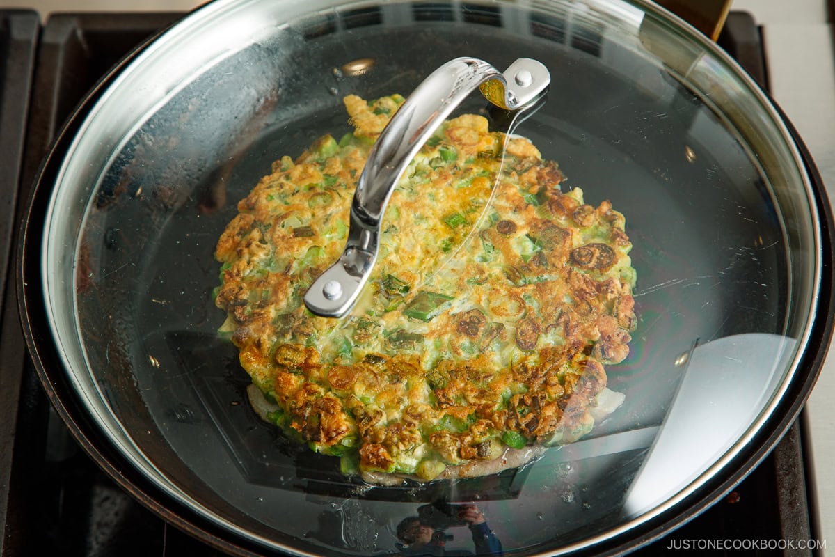 A frying pan containing a negiyaki scallion pancake with the lid on.